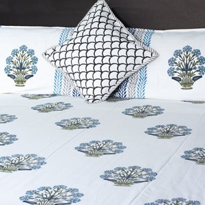 May include: White bed linens with a blue floral pattern and matching pillowcases. The pillowcases have a blue and gray leaf design on the edges and a blue floral design in the center. A square pillow with a black and white scale pattern is also included.