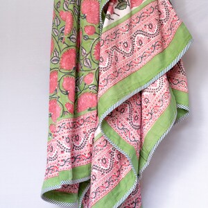 May include: A floral patterned textile featuring large pink flowers and green leaves on a light green background. The border is a contrasting green with a white and blue striped trim. The textile is folded, revealing a pink and white patterned interior.