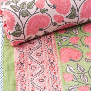 May include: A folded textile featuring a floral pattern in pink and green. The design includes large pink flowers with green leaves on a white background. A green textile with a floral border is also visible.