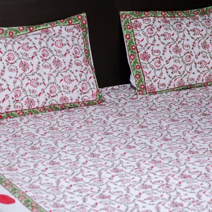 Op de afbeelding: Witte beddengoedset met een rood bloemmotief en groene randen. De set bevat twee kussenslopen en een hoeslaken. Het bloemmotief herhaalt zich over het gehele oppervlak van het beddengoed.