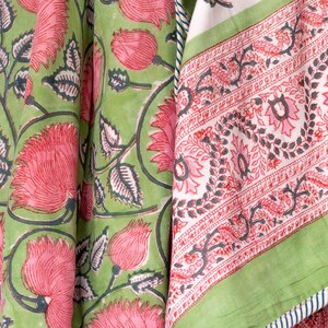 May include: Close-up of fabric with a floral pattern. The fabric features large pink flowers and green leaves on a light green background. A second fabric panel has a white background with a red floral border and green trim.
