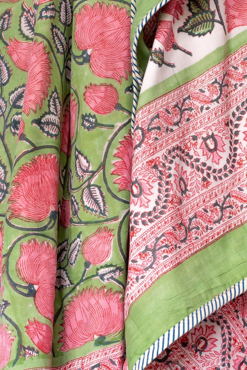 May include: Close-up of fabric with a floral pattern. The fabric features large pink flowers and green leaves on a light green background. A second fabric panel has a white background with a red floral border and green trim.