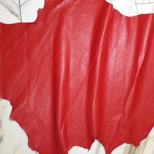 Könnte beinhalten: Ein Stück rotes Leder mit einer glatten, leicht strukturierten Oberfläche. Das Leder ist gefaltet und hat eine natürliche, unregelmäßige Form.