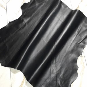 Könnte beinhalten: Ein großes Stück schwarzes Leder, gefaltet und auf einer weißen gefliesten Oberfläche ausgelegt.