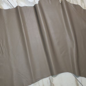 May include: A large piece of light brown leather with a smooth, even texture. The leather is folded and laid flat on a white tiled surface.