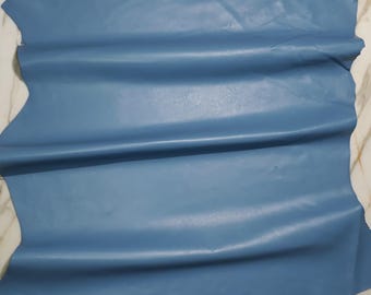 May include: A single piece of blue leather, with a smooth, slightly shiny surface. The leather is a solid, muted blue color, with natural folds and creases. The edges of the leather are uneven, showing its natural shape.
