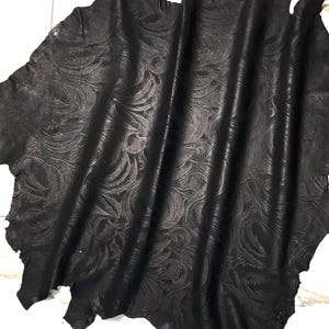 Può includere: Un grande pezzo di pelle nera di forma irregolare con un motivo in rilievo continuo di linee curve vorticose e forme organiche. Il materiale ha una finitura opaca con sottili variazioni tonali create dalla profondità della trama in rilievo.