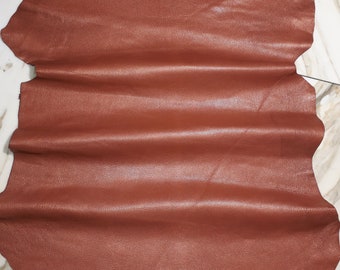 May include: A piece of brown leather with a textured surface. The leather is folded in several places, showing the texture and color.