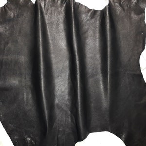 Può includere: Un pezzo di pelle nera con una superficie liscia e leggermente strutturata. La pelle è piegata e drappeggiata, mostrando la sua flessibilità.