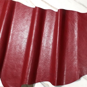 May include: A sheet of red leather with a textured surface. The leather is folded, creating vertical ridges. The colour is a deep, rich red, and the leather appears to be supple and of high quality.