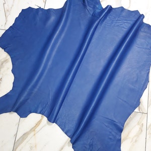 Könnte beinhalten: Ein Stück blaues Leder mit einer glatten, leicht strukturierten Oberfläche. Das Leder ist gefaltet und liegt flach auf einer weißen Fliesenfläche.