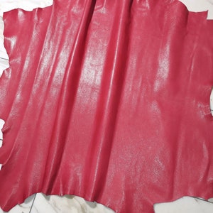Pode incluir: Um pedaço de couro vermelho com um acabamento brilhante. O couro está dobrado e tem uma superfície texturizada.