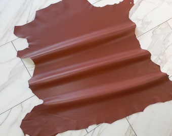 May include: A piece of brown leather with a smooth, slightly shiny finish. The leather is folded in a few places, creating soft, rounded folds.