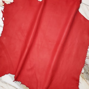 Könnte beinhalten: Ein Stück rotes Leder mit einer rauen, unfertigen Kante. Das Leder ist in der Mitte gefaltet, wodurch ein weicher, fließender Effekt entsteht.