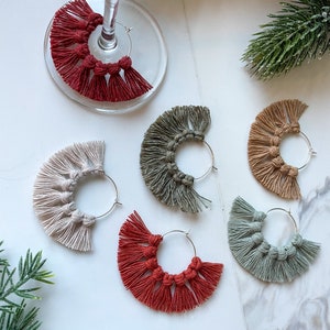 May include: Six pairs of hoop earrings with a fringe of tassels. The earrings are in various colors, including red, green, beige, and gray.