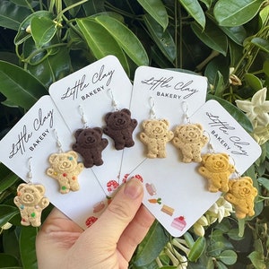 May include: Four pairs of bear-shaped cookie earrings on white cards with the text "Little Clay Bakery". The earrings are in three different colours: brown, tan, and light tan with sprinkles.