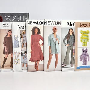 May include: A collection of sewing patterns, including Vogue, McCalls, and New Look brands. The patterns feature images of dresses, suits, and plush animals. The patterns are displayed on a white surface.