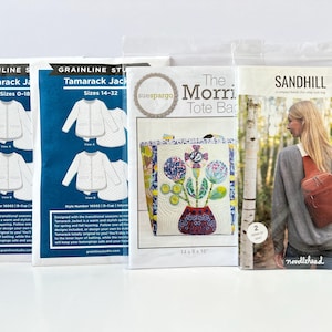 Pode incluir: Quatro pacotes de padrões de costura. Dois padrões de jaqueta Tamarack da Grainline Studio, tamanhos 0-18 e 14-32, e um padrão de bolsa tote The Morri da Sue Spargo. Um padrão de bolsa transversal Sandhill também é visível.