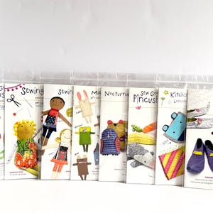 May include: A collection of sewing pattern booklets, each featuring colorful illustrations of dolls, animals, and other crafts. The booklets are packaged in clear plastic sleeves and include the text "Sew G Pincus", "Sewing", "Ma Nocturna", "Kitchen", and "Quilted Slippers".