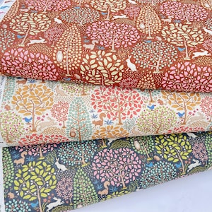 Może przedstawiać: Trzy ułożone na sobie rolki materiału z powtarzającym się wzorem leśnym. Górna rolka jest brązowa z różowymi i kremowymi drzewami, białymi królikami i ptakami. Środkowa rolka jest biała z pomarańczowymi i czerwonymi drzewami, wiewiórkami i ptakami. Dolna rolka jest granatowa z zielonymi drzewami i białymi królikami.