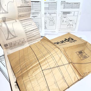 Pode incluir: Uma cole&ccedil;&atilde;o de moldes de costura da Burda Style e rda style. Os moldes incluem diagramas e instru&ccedil;&otilde;es para v&aacute;rias pe&ccedil;as de vestu&aacute;rio. O molde aberto mostra um design de casaco. A embalagem &eacute; branca e castanha.
