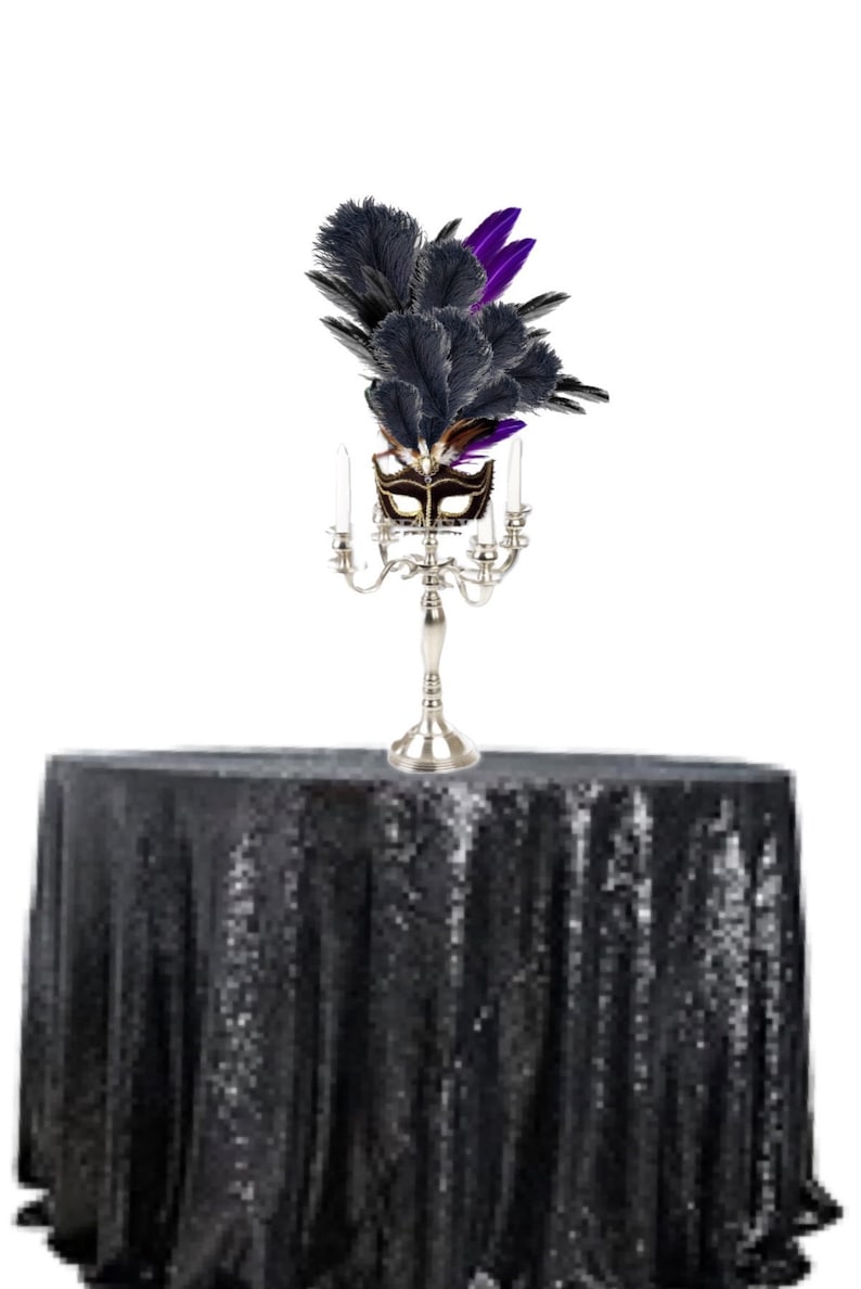 Puede incluir: Un candelabro plateado con cuatro velas encendidas, coronado con una m&aacute;scara de mascarada decorativa y plumas negras y moradas, se encuentra sobre un mantel negro con lentejuelas. La m&aacute;scara es marr&oacute;n y dorada.