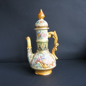 Könnte beinhalten: Eine Keramik-Teekanne mit einem goldverzierten Deckel und Henkel. Die Teekanne ist mit bunten Blumenmustern und goldenen Akzenten verziert.