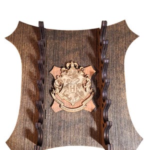 May include: A wooden wall-mounted wand holder with a Hogwarts crest featuring the words "Draco Dormiens Nunquam Titillandus". The holder has 10 slots for wands.
