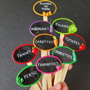 Peut inclure: Un ensemble de neuf marqueurs de jardin colorés avec des étiquettes en ardoise noire. Les étiquettes sont écrites en français et comprennent des noms comme "Pommes de Terre", "Aubergines", "Salades", "Tomates", "Fraises", "Carottes", "Courgettes", "Framboises", et "Persil".