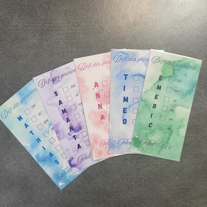 Peut inclure: Cinq cartes colorées avec un fond aquarelle. Chaque carte porte un nom différent, comme "MATHIAS", "SAMANTA", "TIMEO", "ANNA" et "EMERIC". Chaque lettre du nom est accompagnée d'une case à cocher, et un prix est indiqué à côté de chaque case. Le coût total est indiqué au bas de chaque carte.