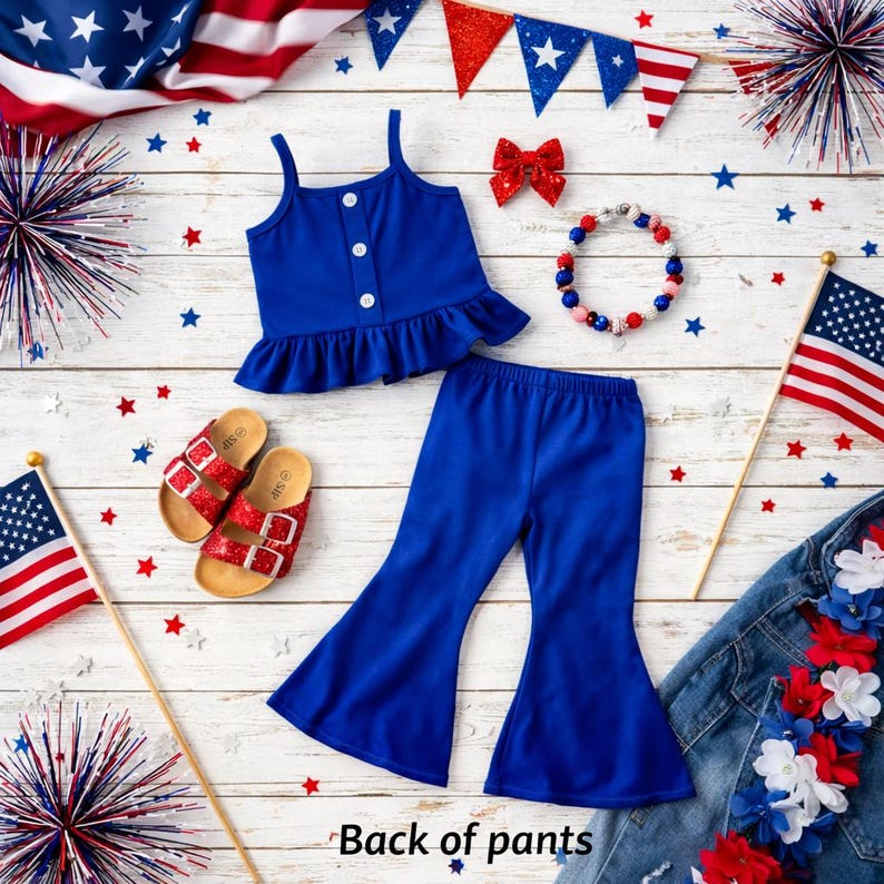 May include: A patriotic ensemble featuring a blue tank top with buttons and a ruffled hem, paired with flared pants. Red glitter sandals, a bow, and a beaded bracelet complement the outfit. American flags and star decorations complete the festive theme.