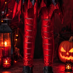 May include: Shiny red leggings featuring horizontal cutouts along the front of the legs, paired with a black and red jagged-hem skirt and black ankle boots with side zippers and white soles, creating a distinct layered appearance.