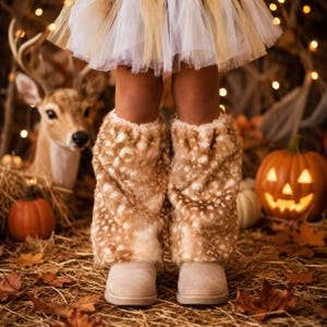 May include: A pair of tan and white faux fur leg warmers with a spotted pattern, worn over light beige boots, paired with a white tulle skirt. The leg warmers feature a soft, plush texture and a loose, gathered fit around the lower legs.