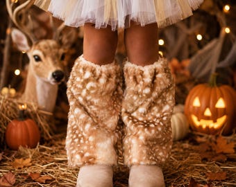 May include: A pair of tan and white faux fur leg warmers with a spotted pattern, worn over light beige boots, paired with a white tulle skirt. The leg warmers feature a soft, plush texture and a loose, gathered fit around the lower legs.