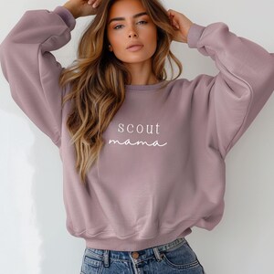 Puede incluir: Una sudadera de color malva con el texto "scout mama" impreso en blanco en la parte delantera.