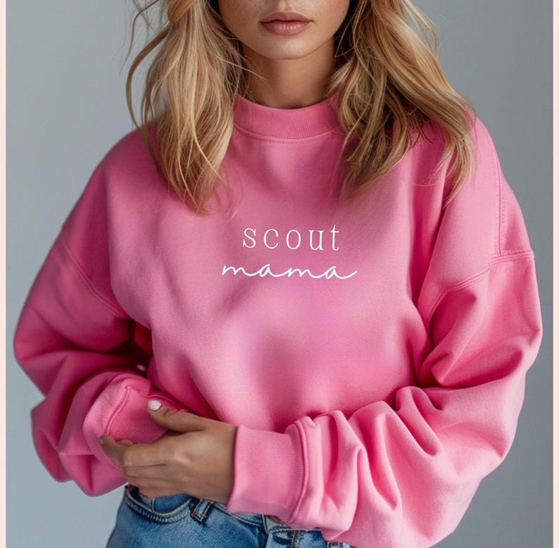 Puede incluir: Sudadera rosa con el texto "scout mama" en letras blancas.
