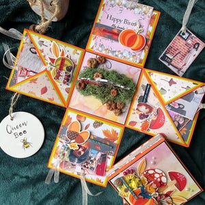 May include: A multi-layered explosion box decorated with autumn-themed paper, embellishments, and photos. The box features a pumpkin, leaves, acorns, and the text "Happy Birthday My Lovely".