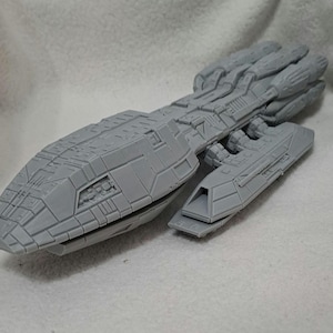 May include: A grey model spaceship with detailed paneling and a textured surface. The spacecraft has a long, rectangular main body with a smaller, attached section. The design suggests a science fiction or fantasy theme.