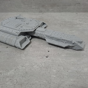 Peut inclure: Maquette grise et détaillée d'un vaisseau spatial. Le modèle présente des panneaux et des éléments de conception complexes, avec un corps central et des ailes étendues. Le vaisseau est en matériau gris clair.