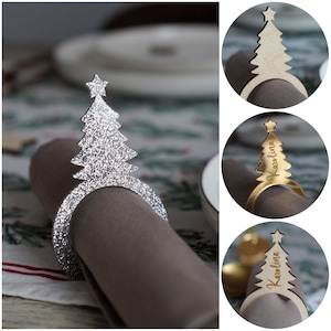 May include: Three silver and gold Christmas tree napkin rings. The silver ring is decorated with glitter. The gold rings have the name "Karolina" engraved on them.