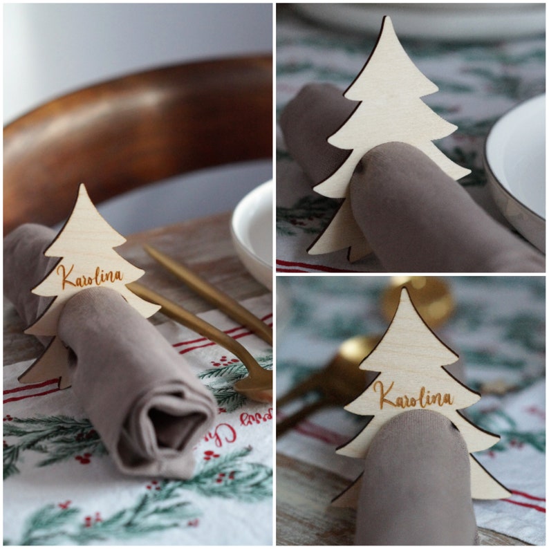 May include: Wooden Christmas tree napkin rings with the name Karolina written on them. The rings are placed on a white napkin with a red and green pattern.