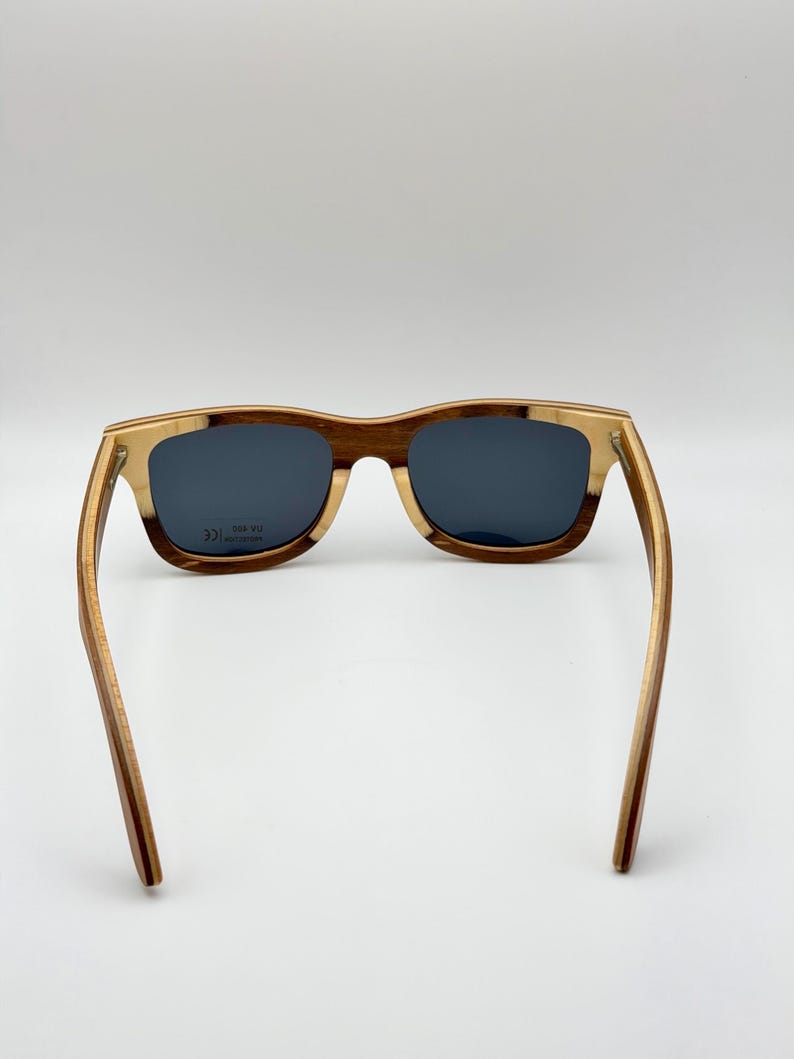 May include: Wooden sunglasses with a rectangular frame. The frame is a combination of light and dark brown wood, with dark lenses. The arms of the sunglasses are extended, showing the full length of the frame.