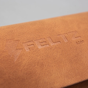 May include: Close-up of a brown leather item with the embossed word "FELTZ" and the word "GOOD". The leather has a textured surface and a warm, natural colour.