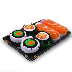 Puede incluir: Una bandeja negra contiene una colorida variedad de rollos de sushi. El sushi incluye rollos con detalles blancos, negros, verdes y naranjas, y dos piezas de nigiri de salmón. El sushi está dispuesto con hojas decorativas verdes.
