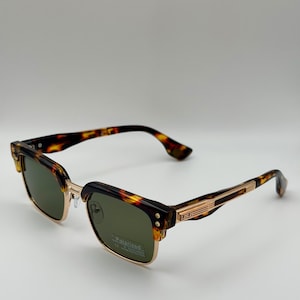 Könnte beinhalten: Quadratische Sonnenbrille mit Schildpattmuster auf dem oberen Rahmen und den Bügeln. Der untere Rahmen und der Steg sind goldfarben. Die Gläser sind grün und der Text "Polarized" ist sichtbar.
