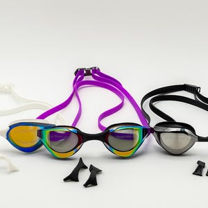 May include: Swimming goggles in white, blue, purple, and black. The goggles have mirrored lenses and adjustable straps. Additional nose pieces are included. Ideal for competitive swimming or recreational use.