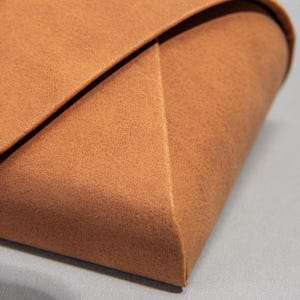 May include: Close-up of a brown, textured, folded object. The object has a geometric shape with a triangular corner and a curved edge. The material appears to be leather or a leather-like material.