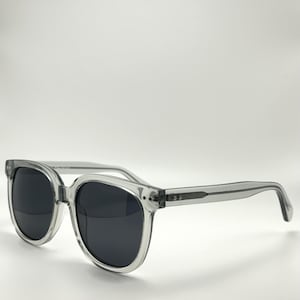May include: Clear frame sunglasses with black lenses. The sunglasses have a square shape and a thin frame.