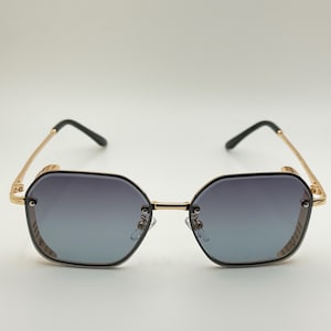 Pode incluir: &Oacute;culos de sol octogonais com arma&ccedil;&atilde;o dourada e lentes degrad&ecirc;. As lentes v&atilde;o do escuro ao claro. As hastes s&atilde;o douradas com pontas pretas. O design &eacute; moderno e elegante. A largura da arma&ccedil;&atilde;o &eacute; de cerca de 14 cm.
