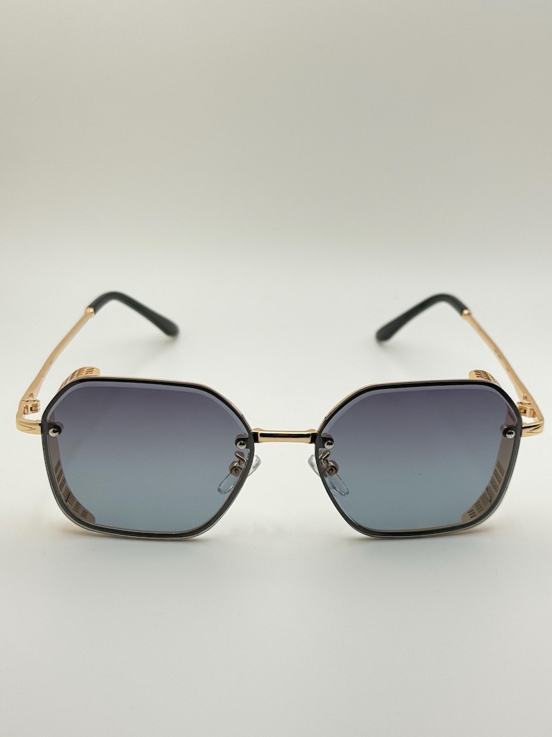 Pode incluir: &Oacute;culos de sol octogonais com arma&ccedil;&atilde;o dourada e lentes degrad&ecirc;. As lentes v&atilde;o do escuro ao claro. As hastes s&atilde;o douradas com pontas pretas. O design &eacute; moderno e elegante. A largura da arma&ccedil;&atilde;o &eacute; de cerca de 14 cm.